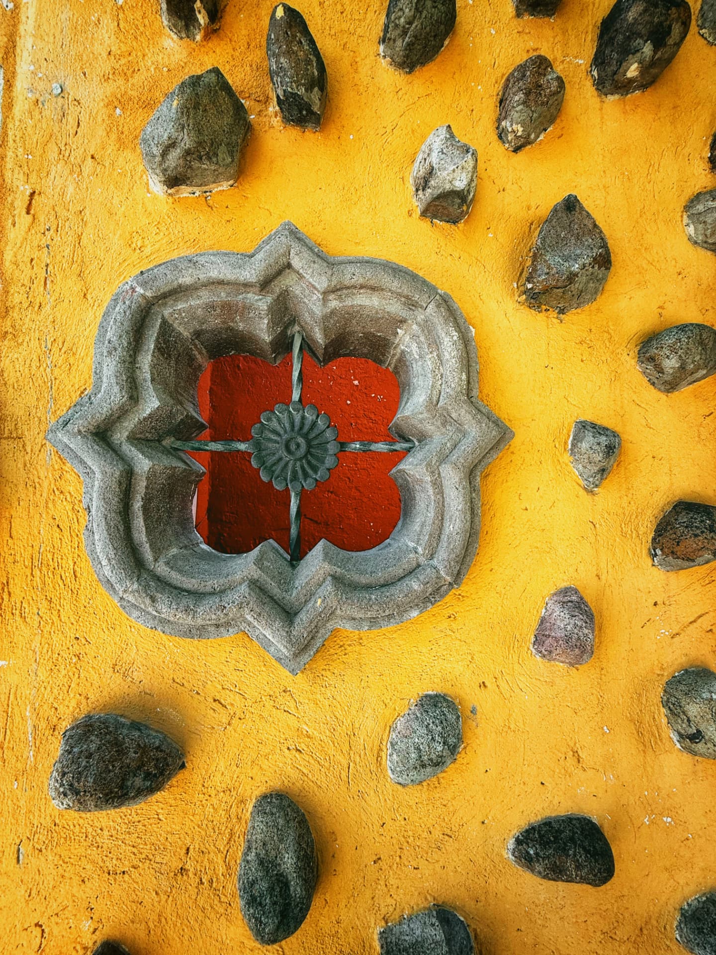 Found detail on a bright yellow wall with stone and carved shapes in San Luis Potosi, Mexico