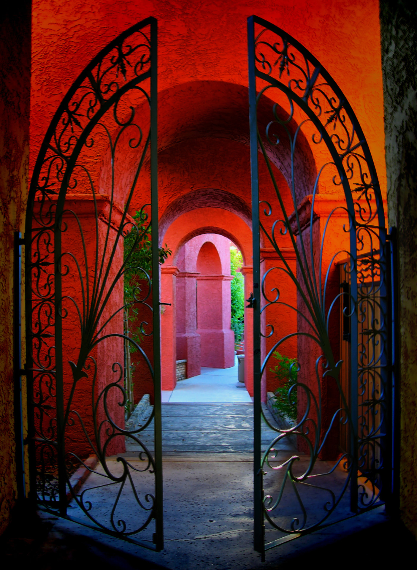 Ornate iron gate opening onto a red adobe passageway